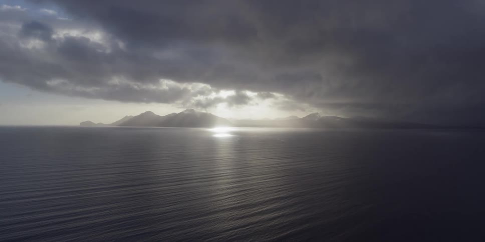 The sun sets over mountains and the sea