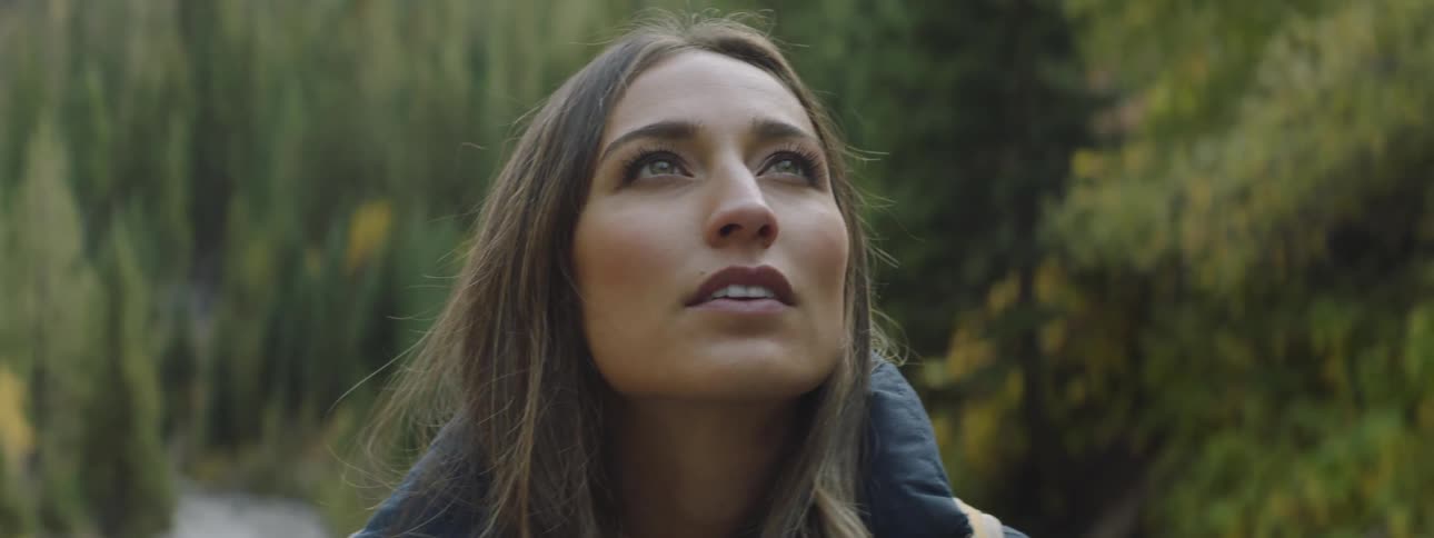 A woman wearing a backpack in the woods looks up
