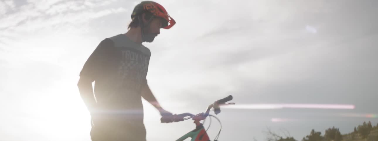 Man picking up his bicycle and riding it in a barren area at sunset on a cloudy evening
