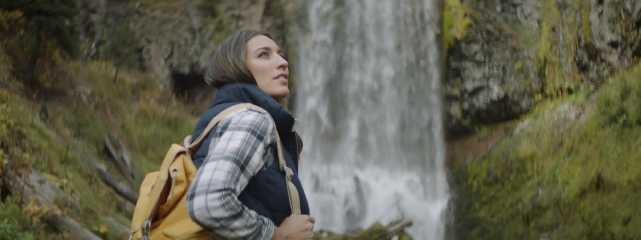 A woman stands and looks around as water falls off the cliff
