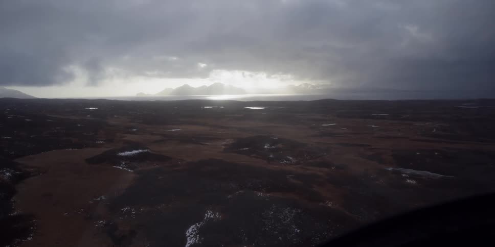The sun is casting a spot of light through storm clouds onto the ocean