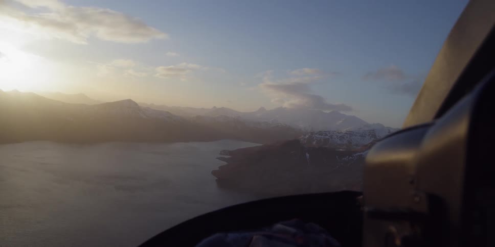 An aircraft flies over a lake and snowy mountains at sunset
