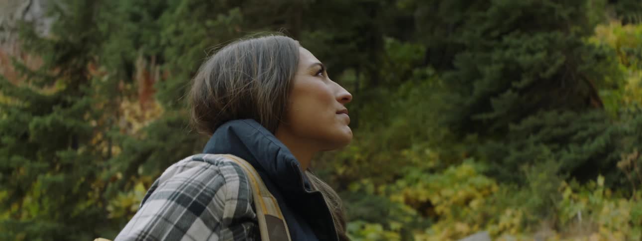A woman is standing in a natural setting looking around at her surroundings