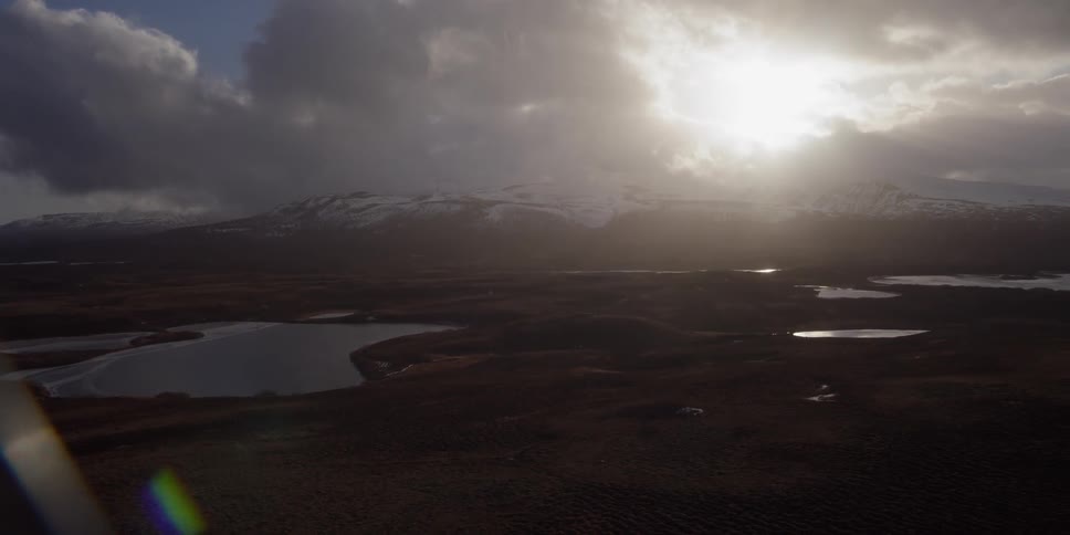 The sun is peeking through clouds as they move over a mountain coastline
