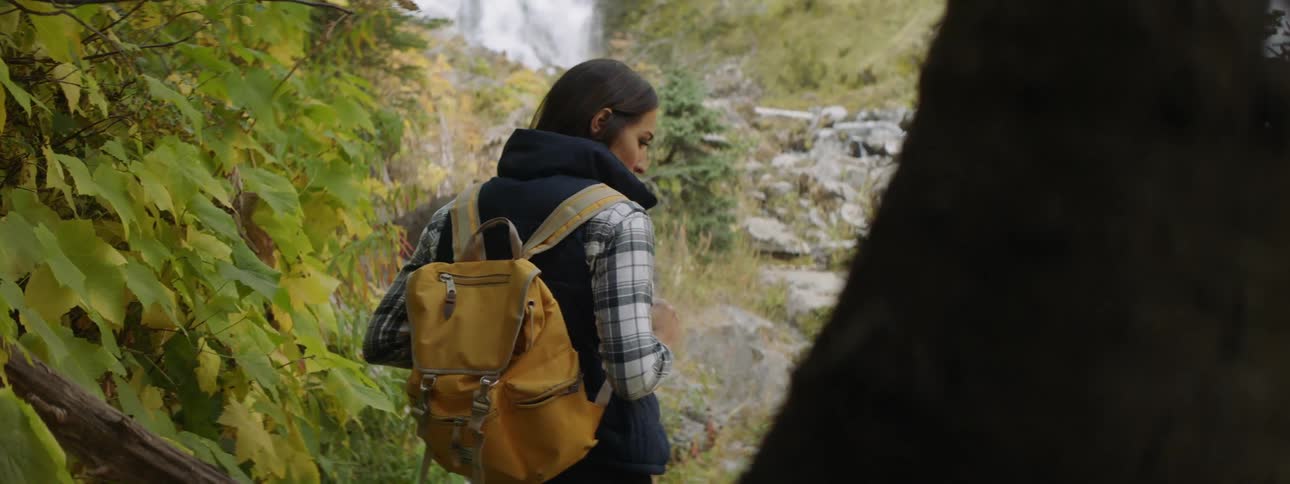 A woman with a backpack is standing in front of waterfall