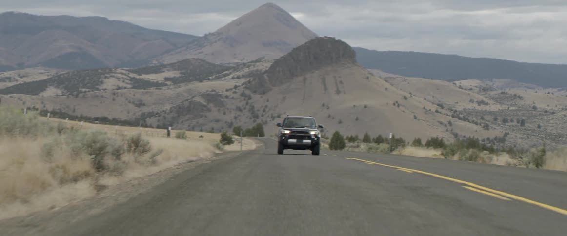 A car drives down the long road near the desert
