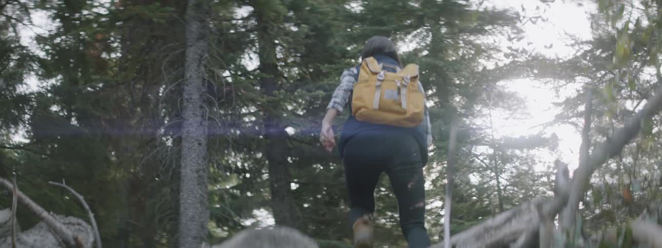 Woman wearing a yellow backpack walks through the woods