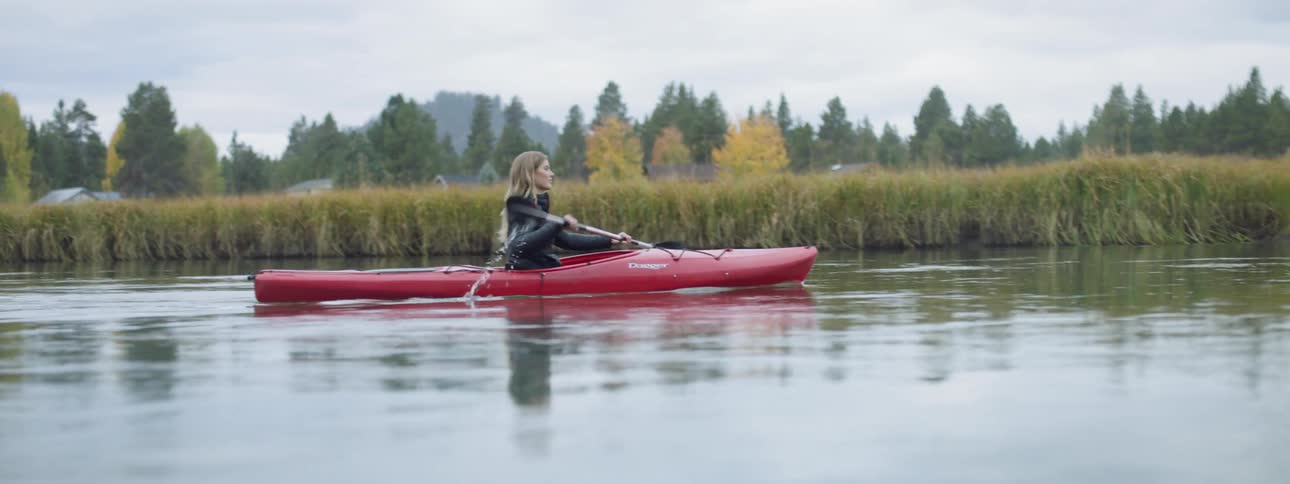 A woman is paddling a red canoe down a small river