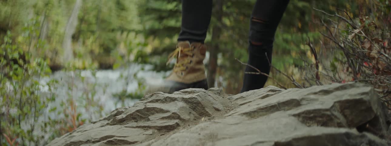 Woman walks in the woods and steps up on a big rocks