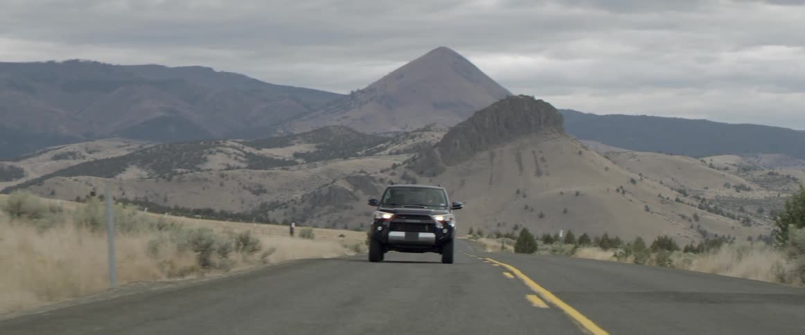 A vehicle drives on a rural road with mountains in the distance