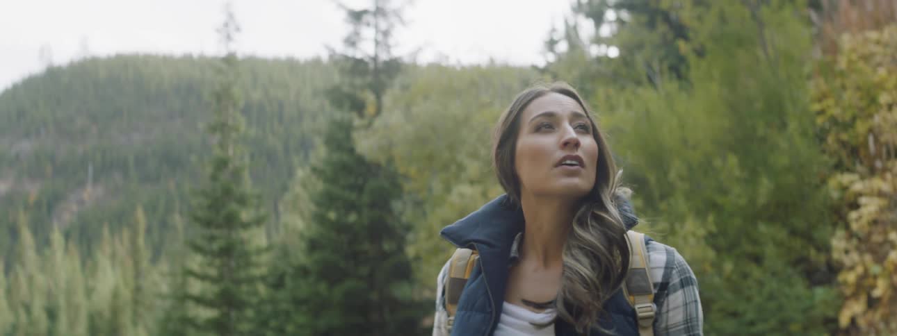 Woman walks through the woods wearing a yellow backpack