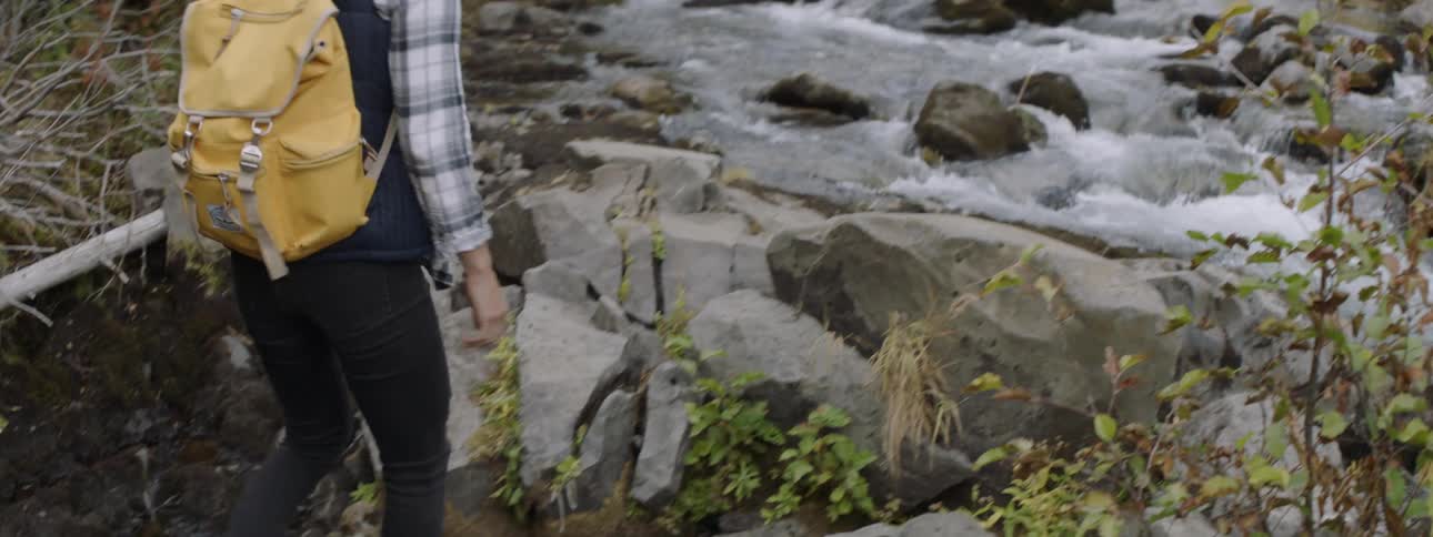 A woman walks on rocks by the stream