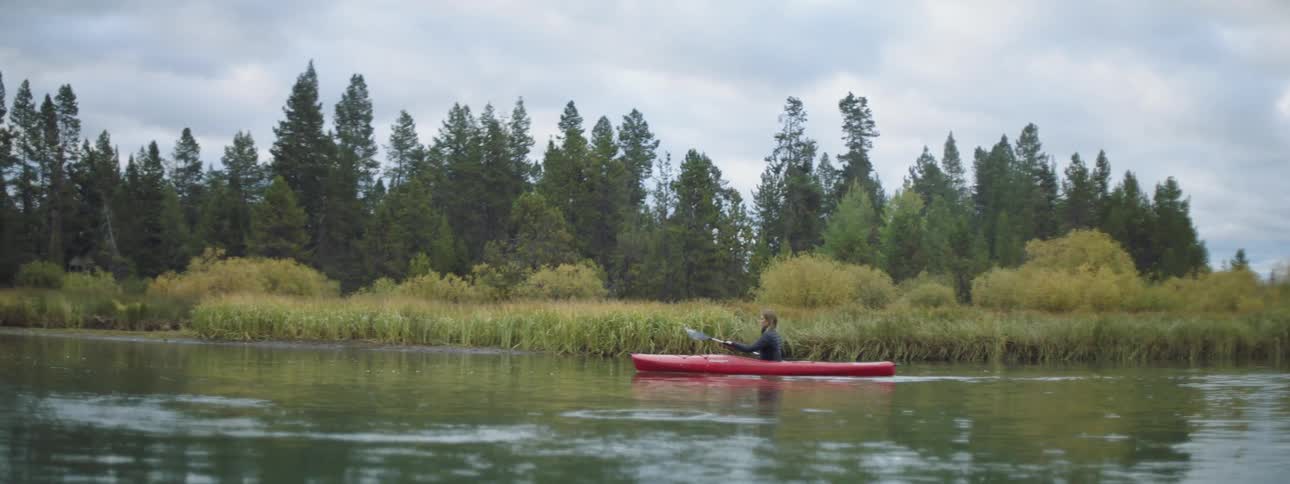 Woman paddles a red kayak down a river