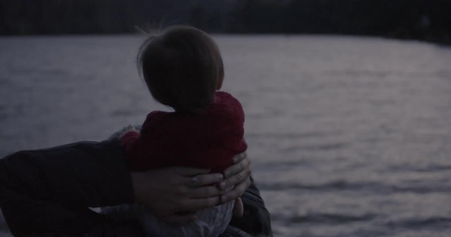 A dad holds his daughter on his shoulders as they look out at the water