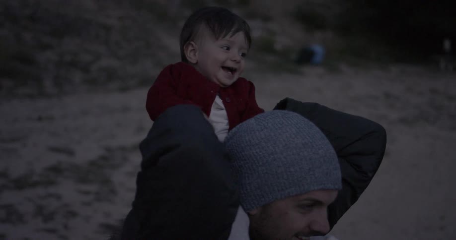 A small child is sitting on the shoulders of his dad at the beach