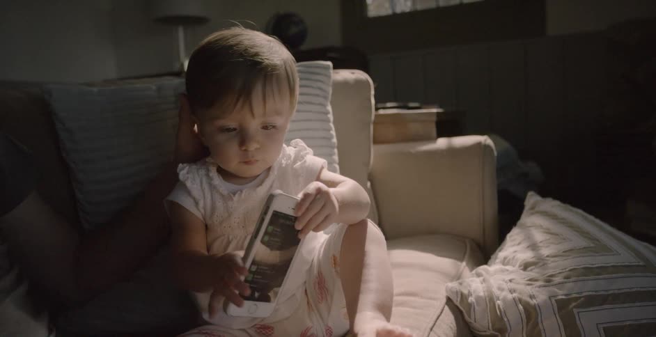 A young child holds a cell phone while on the couch