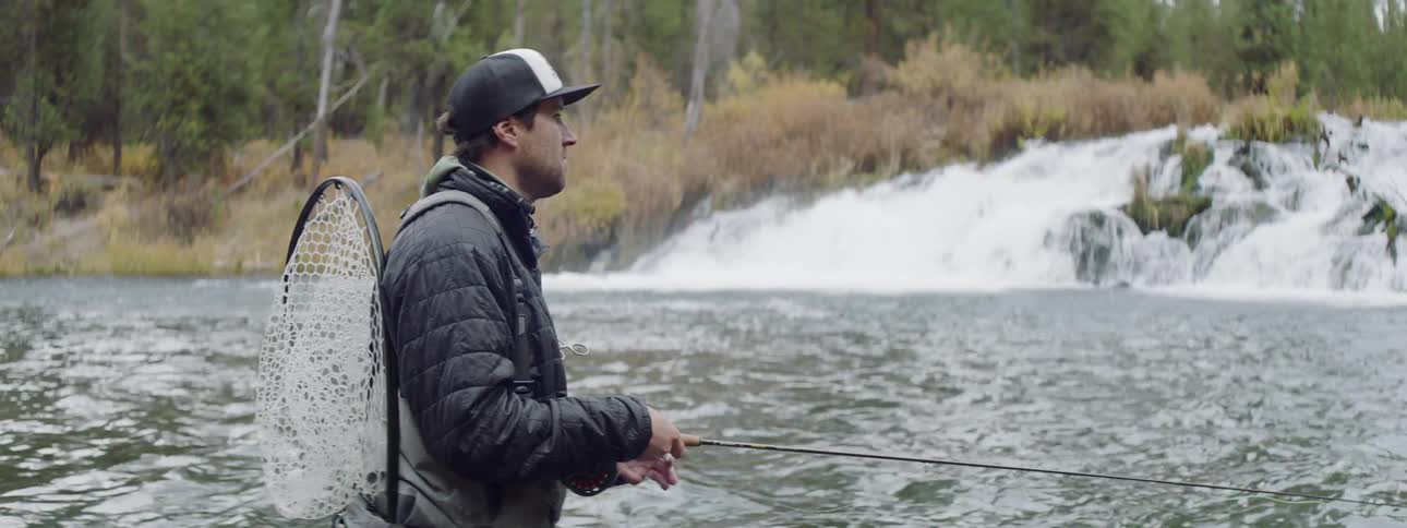 A man is fishing in the rough stream waters