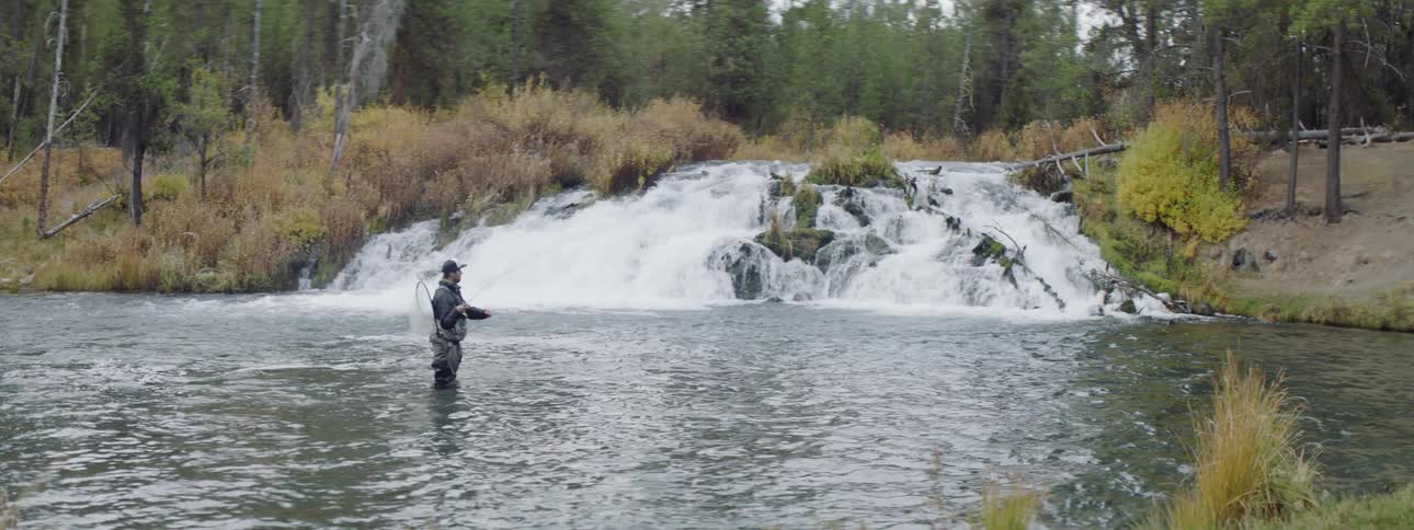 A man is casting his line as he fishes in a river during the day