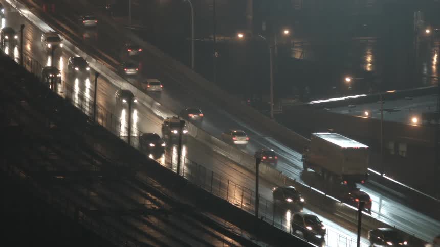 Vehicles drive on a wet city road at night