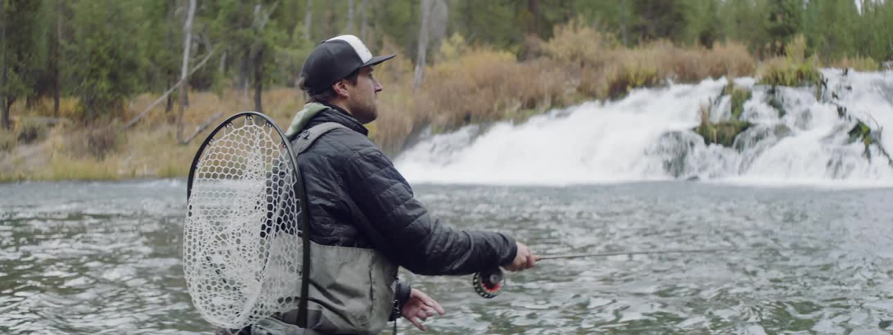 A man is casting out his fishing line as he fishes in a river during the day