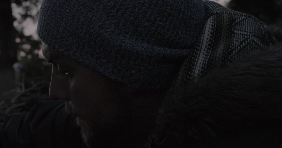 Man kneels down in the woods near a fallen tree