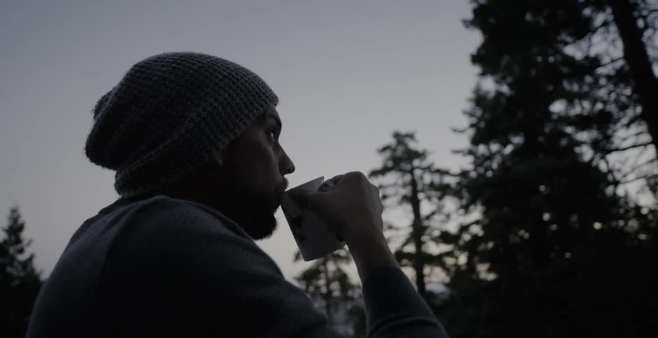 Man drinks coffee in a forest at sunrise