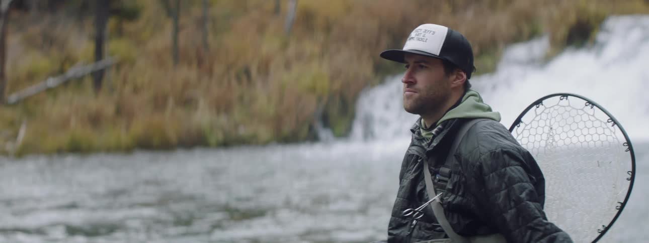 A man is standing next to a stream fishing