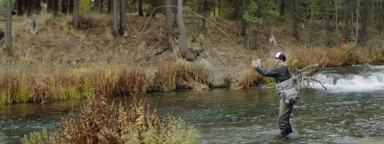 A man is fishing in the water leaning forward
