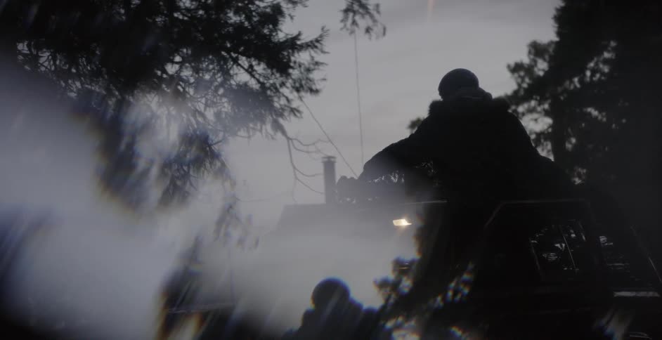 A man is securing a christmas tree to the top of his suv at dusk