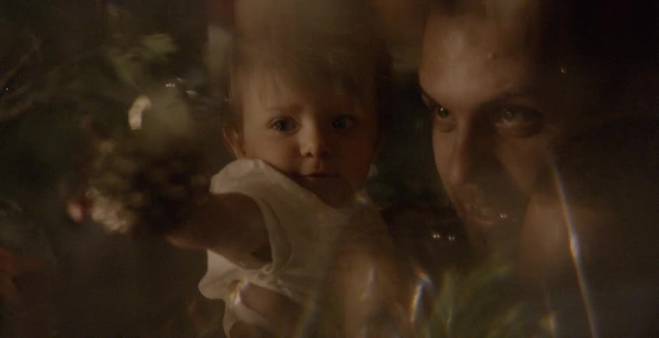 A dad holds his daughter as she reaches for an ornament on the tree