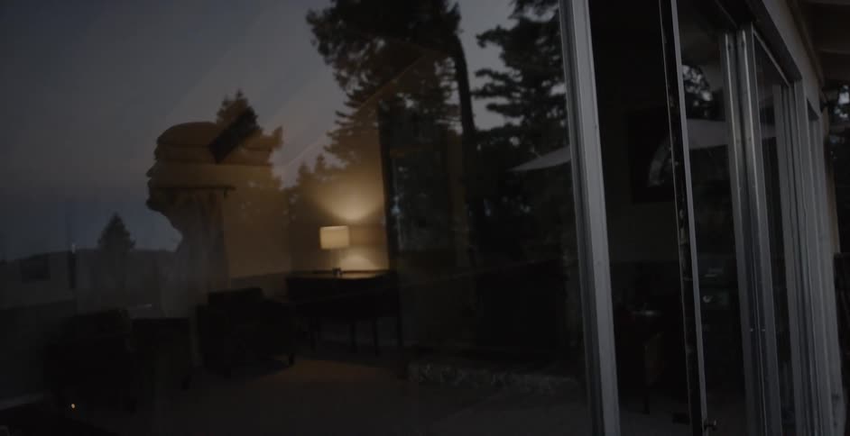 A man's reflection is seen in a window at dusk