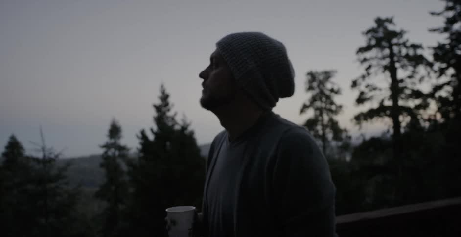 Man looking upward in a wooded area as he carries his drink