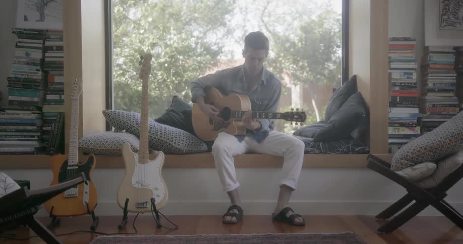 A man plays acoustic guitar on a window bench