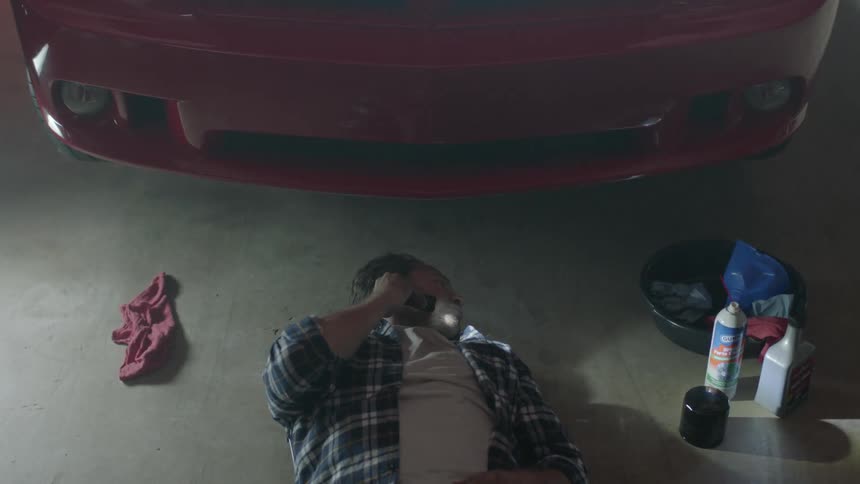 Man holding a flash light pulls himself out from underneath a red car