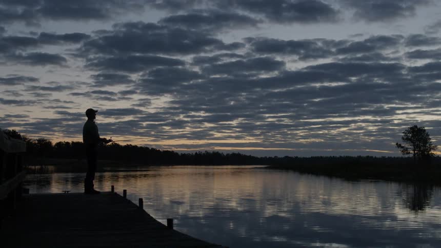 A man is fishing in a lake at dusk