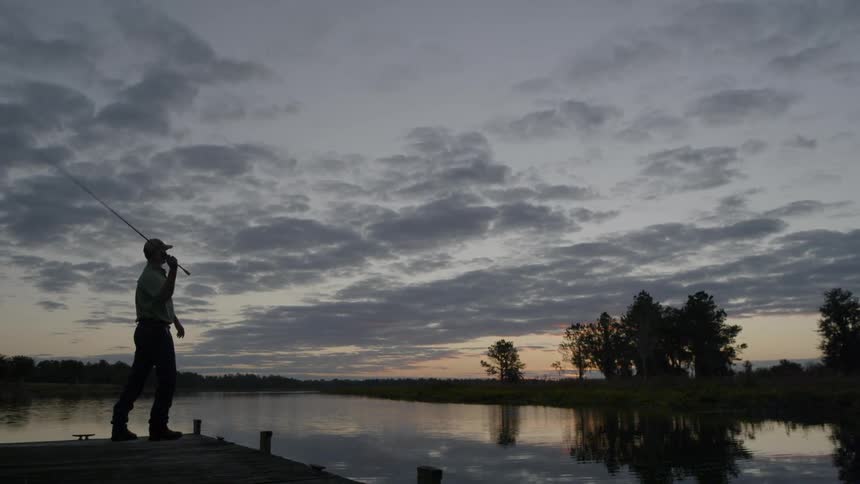 A man fishes off a dock at sunrise