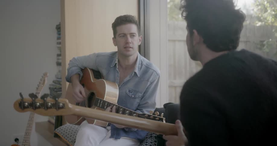 Two men singing and playing their guitars indoors