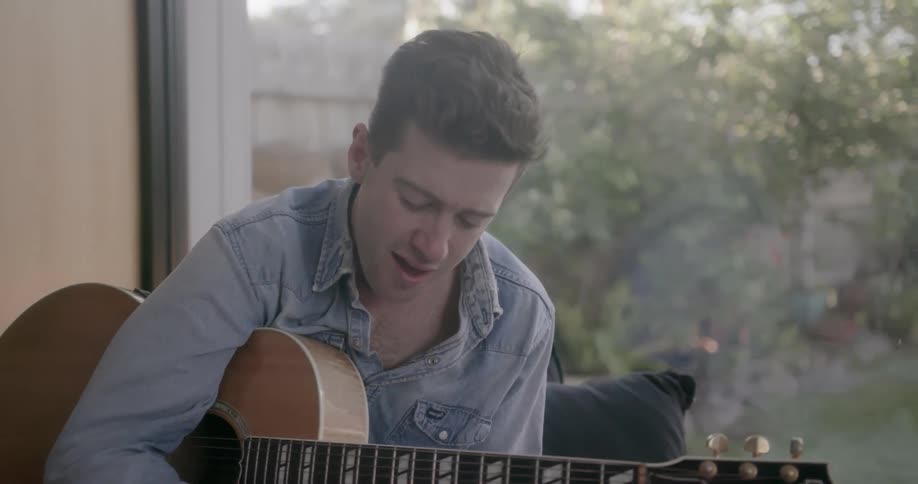 A guitarist composes music while sitting on a window bench
