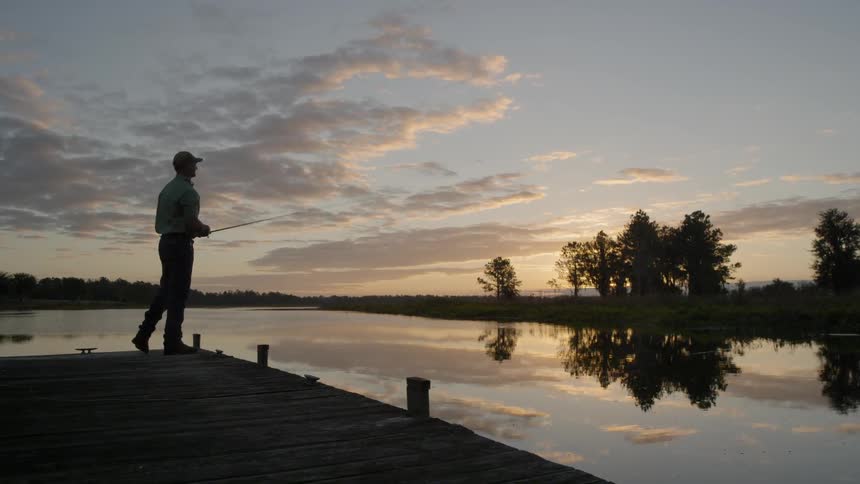 Man fishes off a dock at sunset