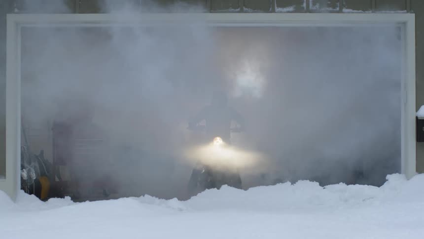 A man revs a motorcycle in an open garage on a snowy day
