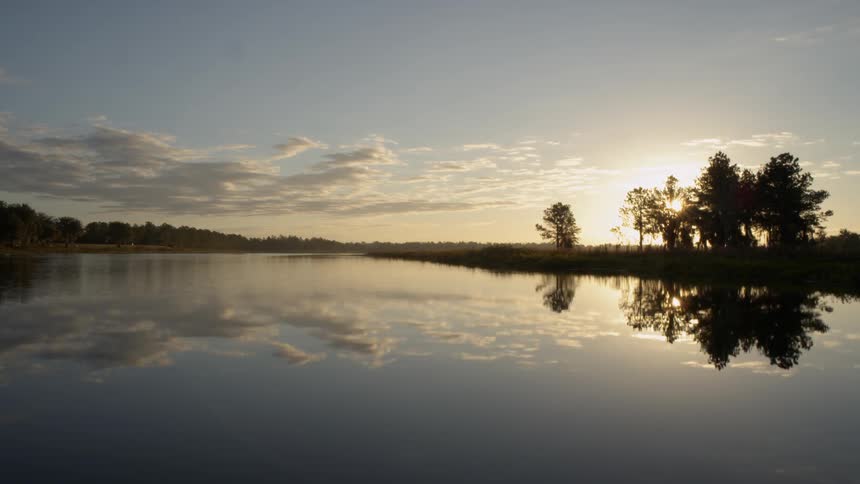 The sun sets and shines on a lake