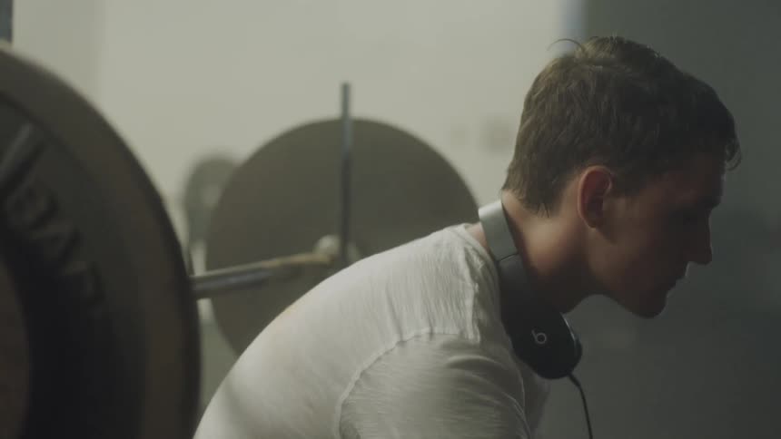 Man with headphones around his neck is sitting down on a weight bench