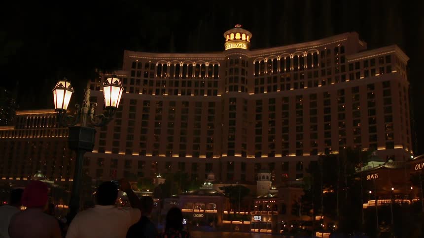 People are taking photos of a fountain display in front of a las vegas casino at night