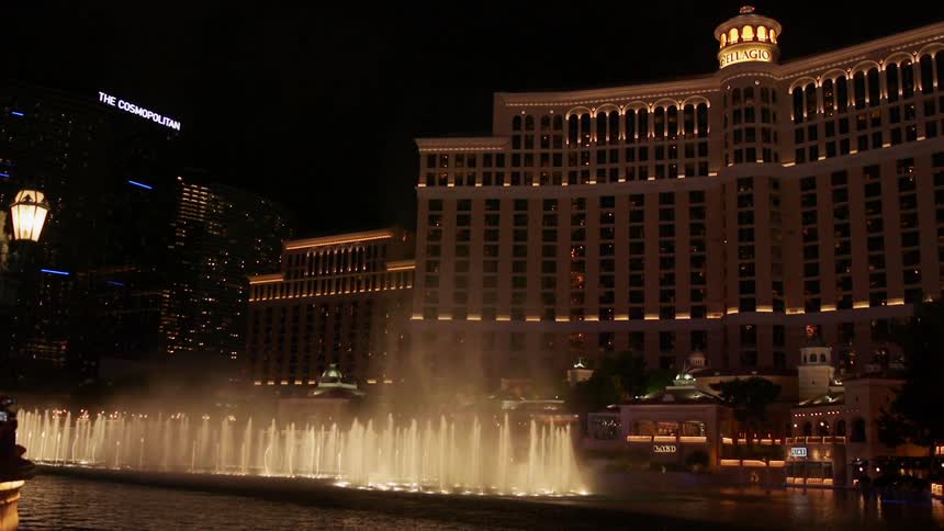 Water fountains spray up in front of a hotel at night