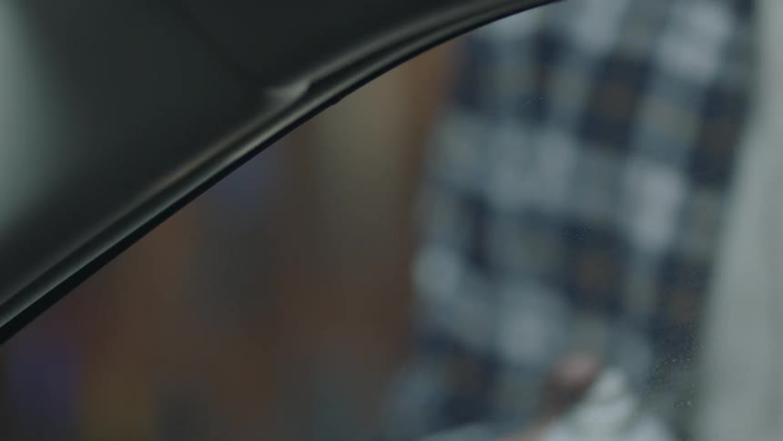 A person sprays cleaner on a car window then wipes it clean
