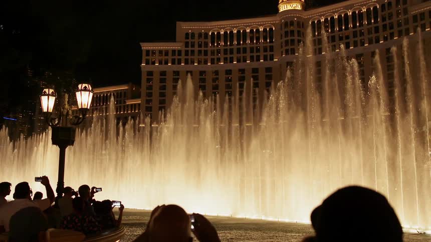 People are taking photos of a fountain display in front of a las vegas casino at night