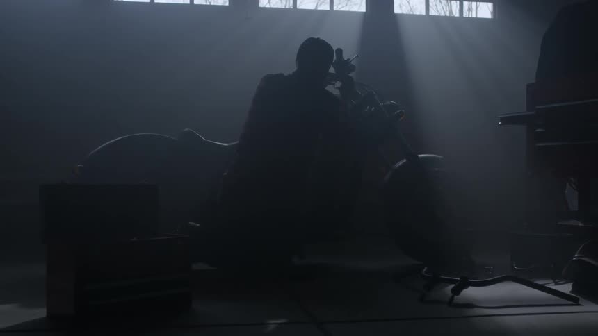 A man is working on his motorcycle inside a garage during the day