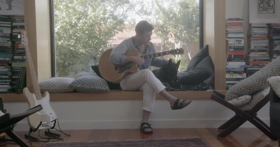 A man is petting his dog and holding a guitar