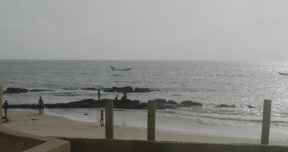 People walk on the beach as a boat rides on the water