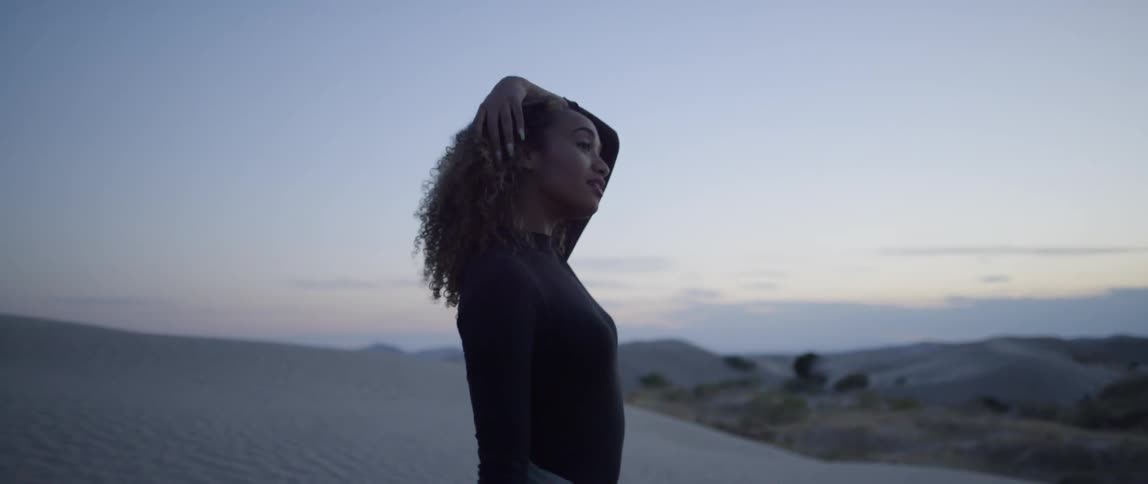 A woman walks in a desert at sunset